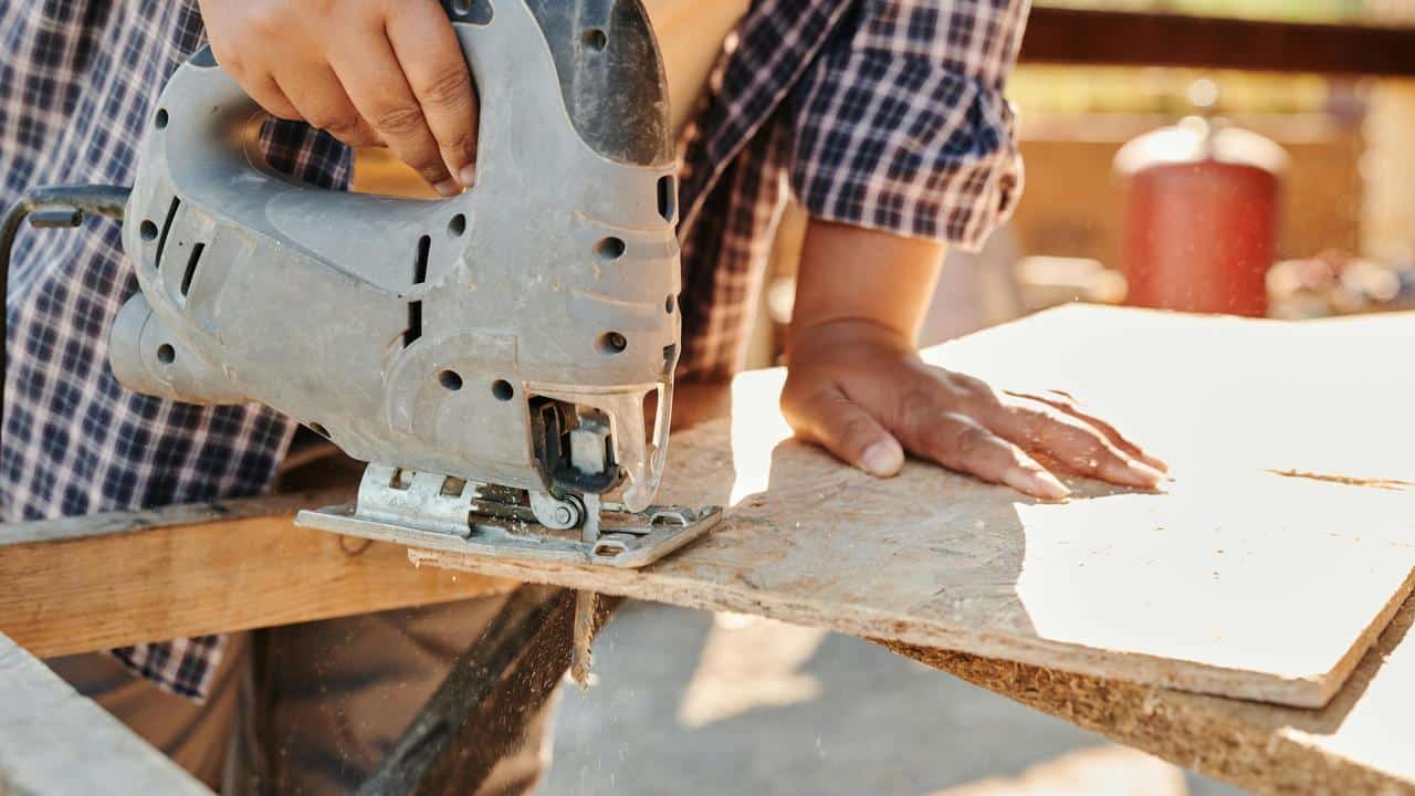 A person using a jigsaw to cut a piece of wood outdoors.