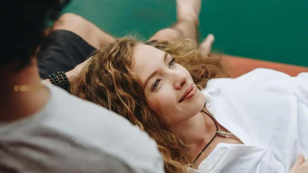 A woman with curly hair lying down and smiling softly.