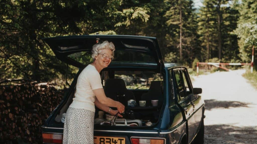 A woman placing a bag in the trunk of a car.