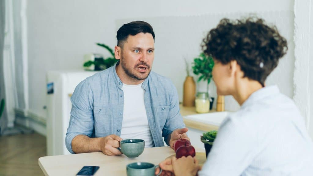 An angry man sitting at a table talking to a woman.