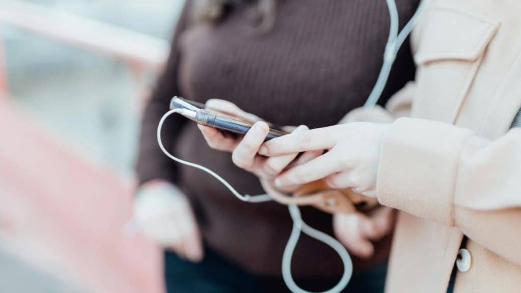 A close-up of two people holding a smartphone together with earphones plugged in.