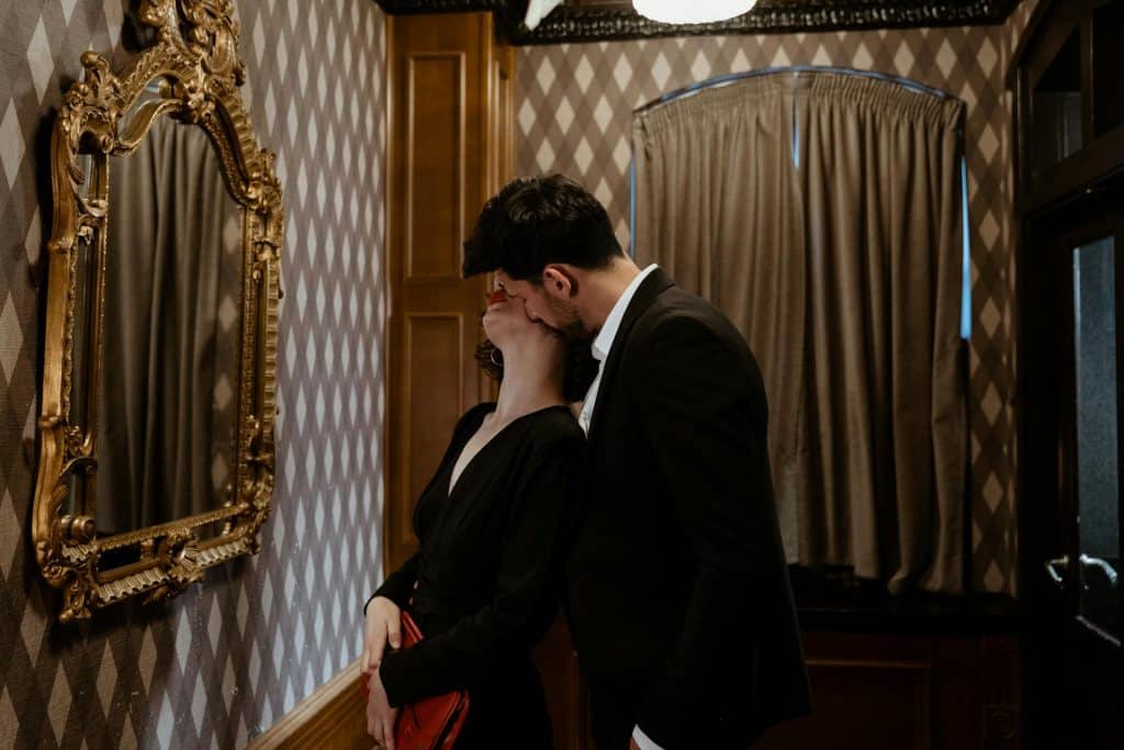 A man in a black suit kissing the woman on the neck.