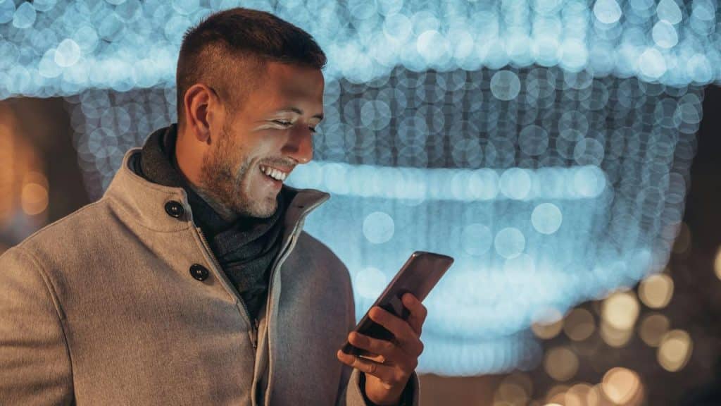 A man smiling while looking at his smartphone outdoors at night