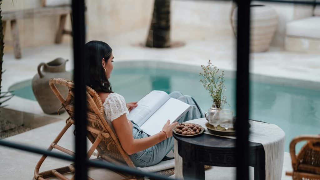 A woman sitting by a pool reading a book at a small table.