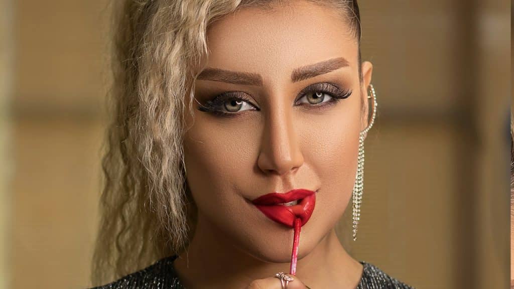 A woman in a black sweater applying lip gloss on her lips.