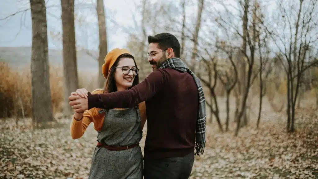 A couple smiling and dancing together in a forest.