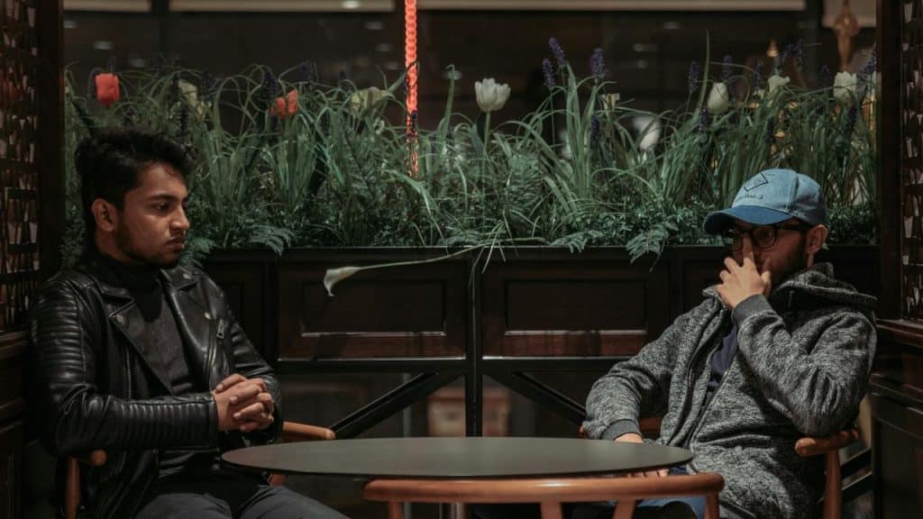 A pair of men sitting at a small table, appearing to have a serious conversation
