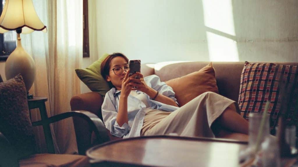 A woman in glasses lounges on a couch looking at her phone indoors.