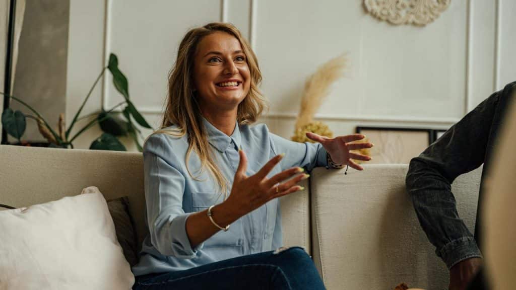 A woman smiling and gesturing while talking on a couch.