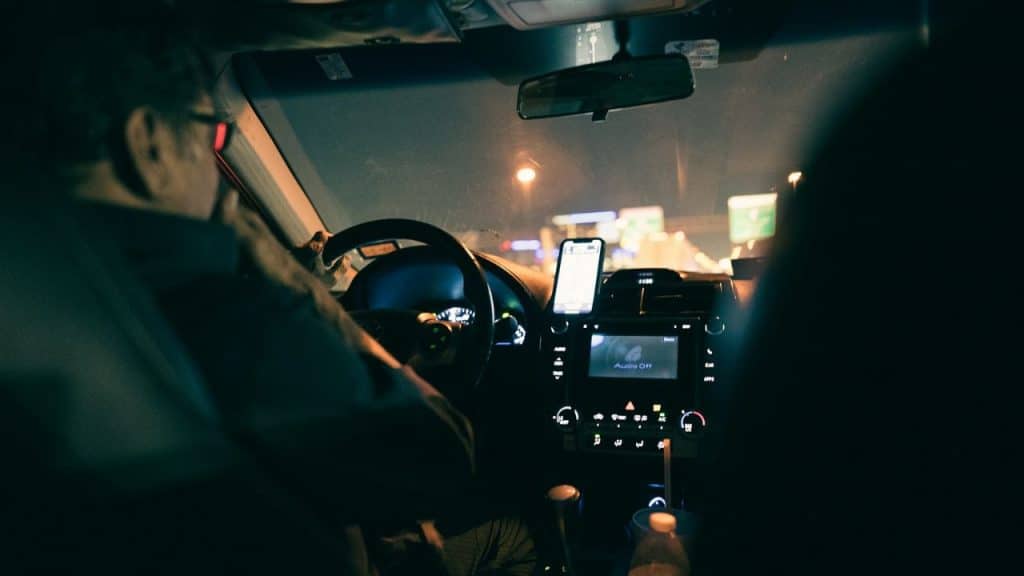 Interior view of a car at night showing the driver and the dashboard with a mounted phone.