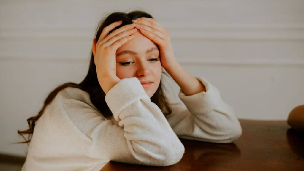 Young woman sitting at a wooden table with her head in her hands.
