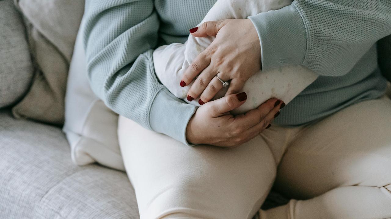 A person sitting on a couch holding a baby wrapped in a blanket.