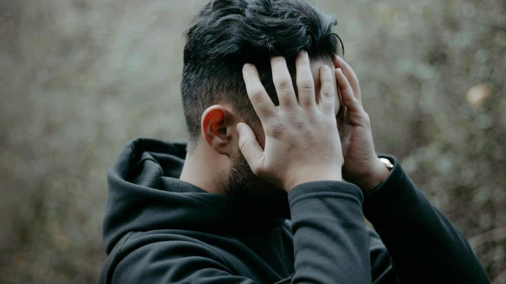 A man outdoors holding his head with both hands.