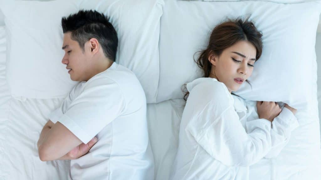 An overhead view of a couple in bed, both facing away from each other looking upset.