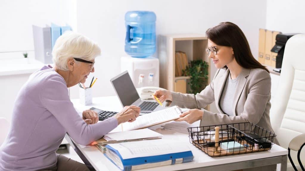 A young female agent helping a senior client to fill in an insurance document.