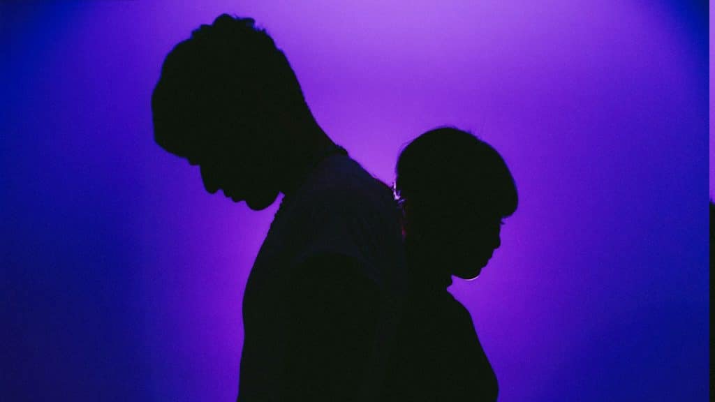 A silhouette of a couple standing close while looking downwards.