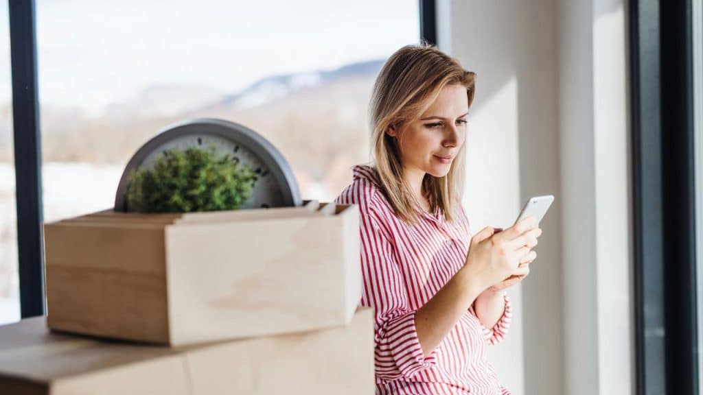 A woman standing by a window using a smartphone.