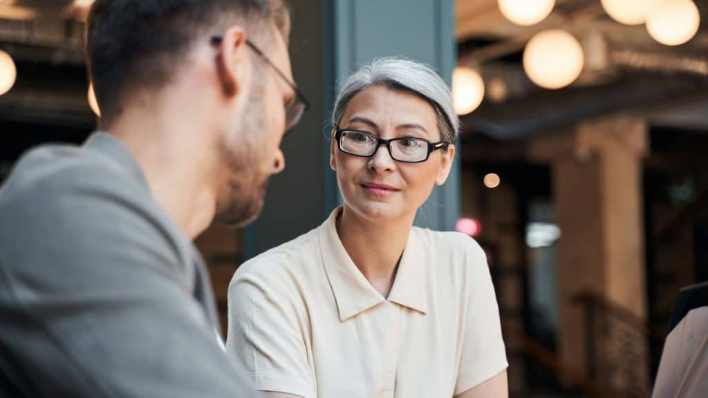 Woman in glasses and light collared shirt looking intently at a man.