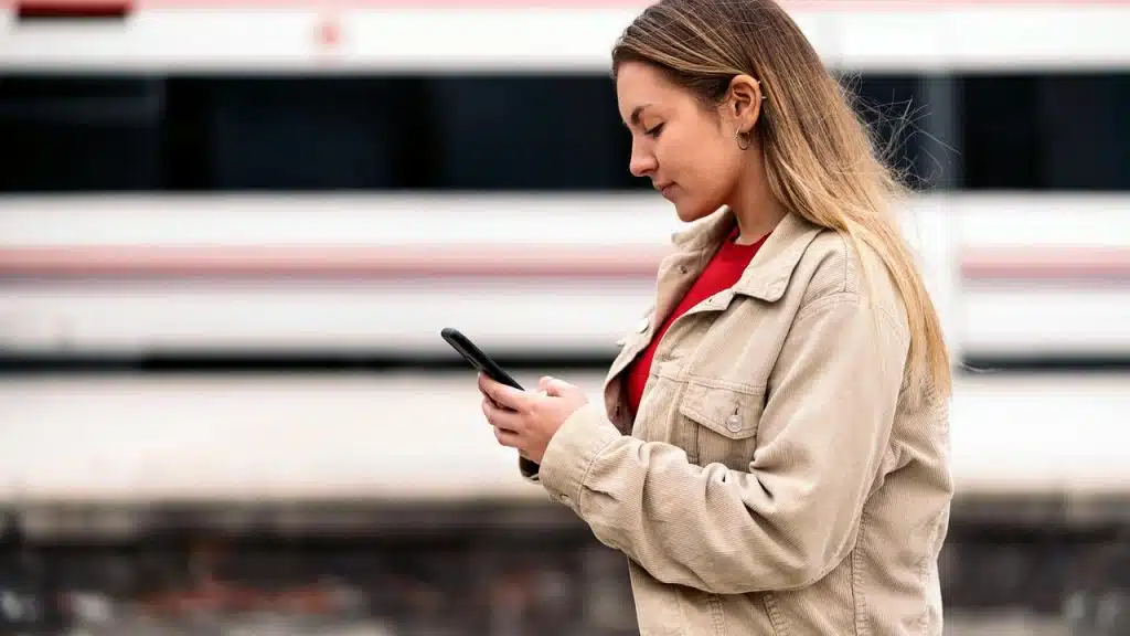 A woman standing outdoors looking at her phone.