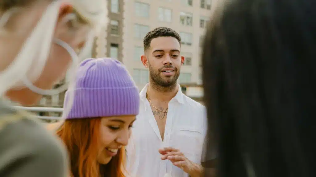 A man with a subtle smile talks to three people outdoors in a city setting.