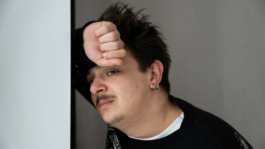 Young man with short hair and earrings resting his fist on his forehead.