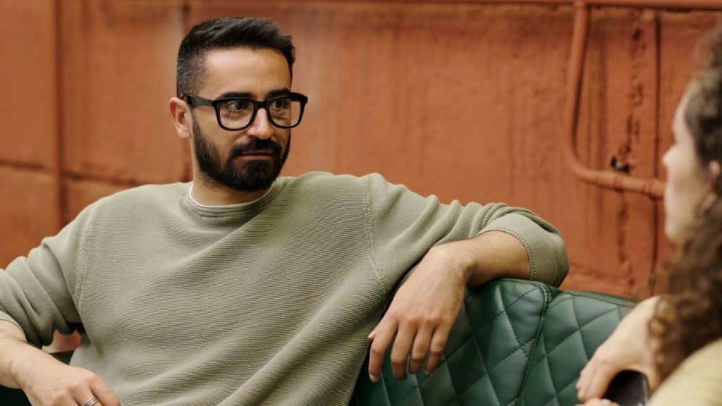 Man with a beard and glasses in a light green shirt talking to a person.