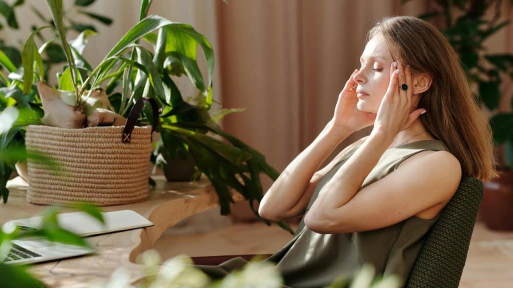 A woman sitting at a desk with her eyes closed, massaging her temples in stress.