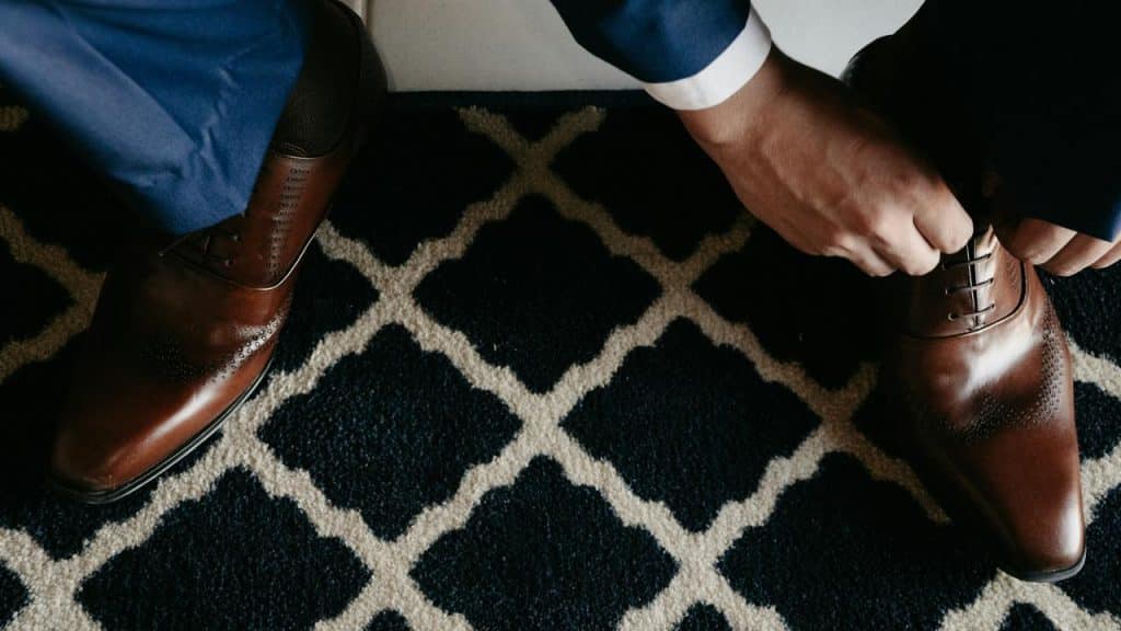 A man in a suit tying the laces of his brown dress shoes.