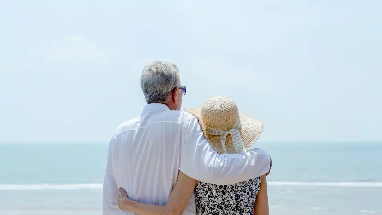 An elderly couple embracing while looking at the ocean.