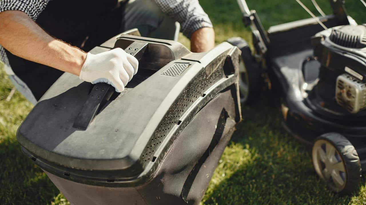 A person wearing gloves handling a lawn mower on the grass.