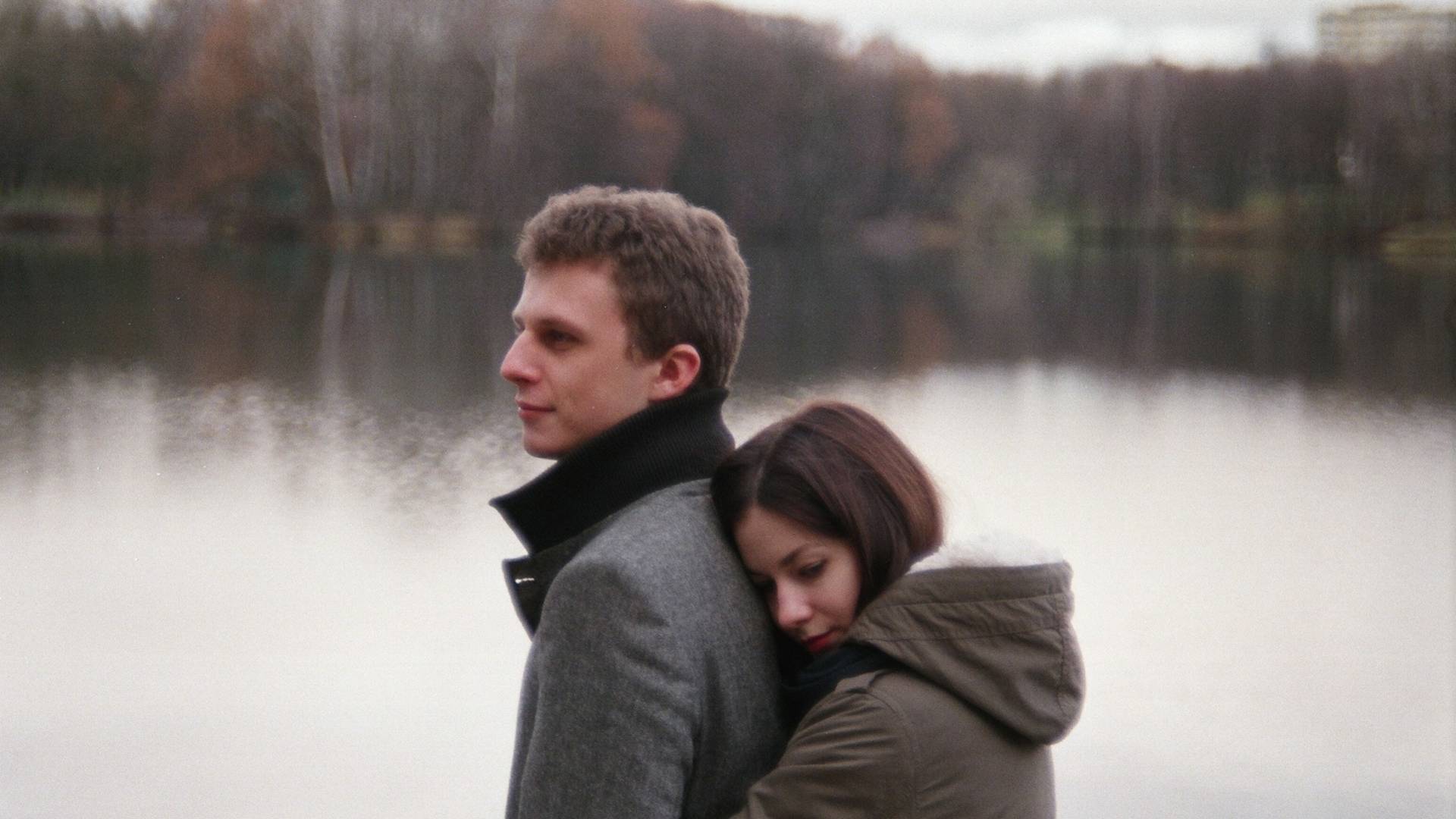 A woman hugging a man near the lake.