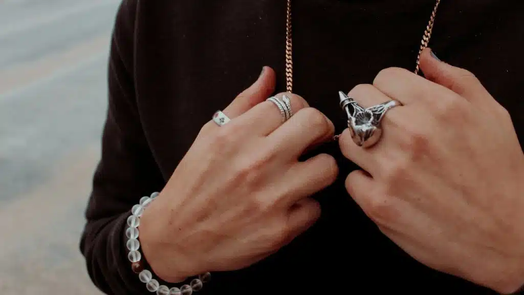 Close-up of hands wearing multiple silver rings, a chain necklace, and a beaded bracelet.