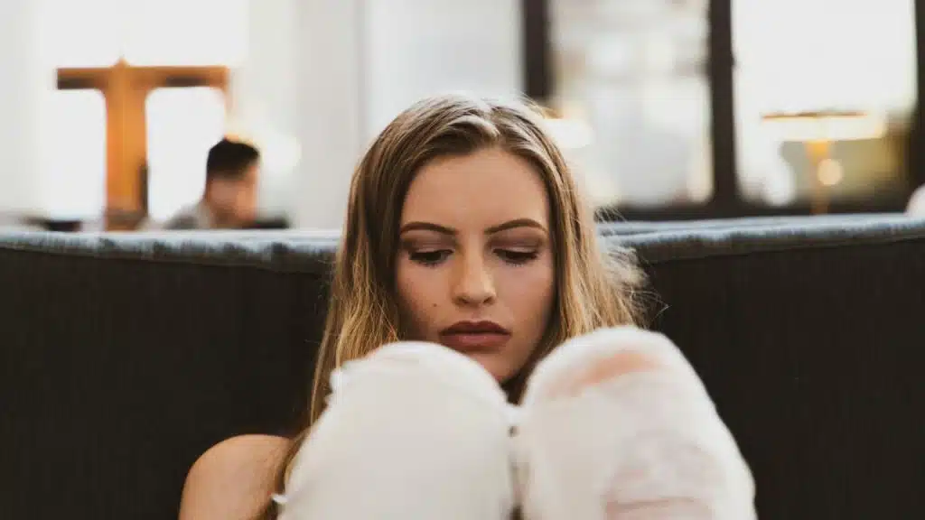 Woman with long blonde hair looking down while hugging her knees on a couch.