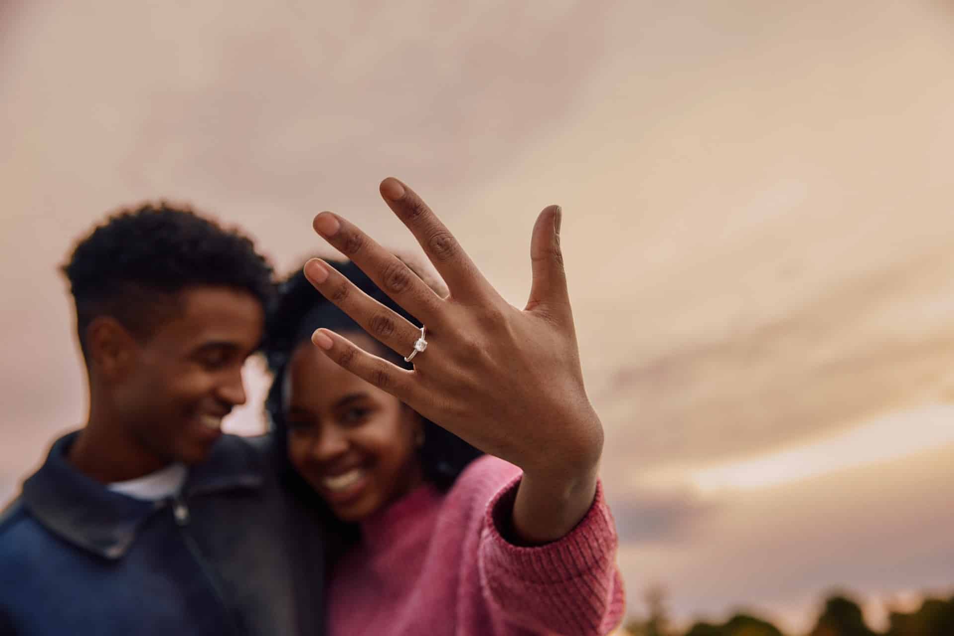 A man looking at the woman who’s showing off her engagement ring.