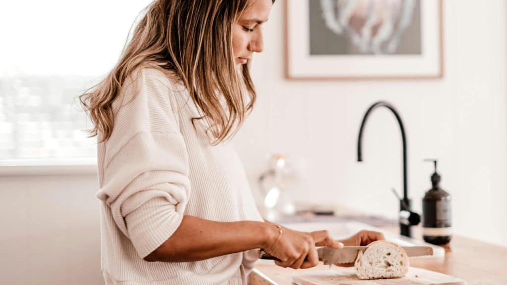 A woman slicing a loaf of bread in a bright kitchen.