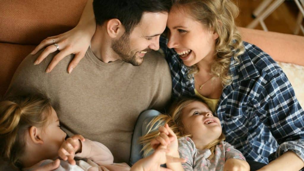 Happy family of four on a couch, smiling and laughing together indoors.