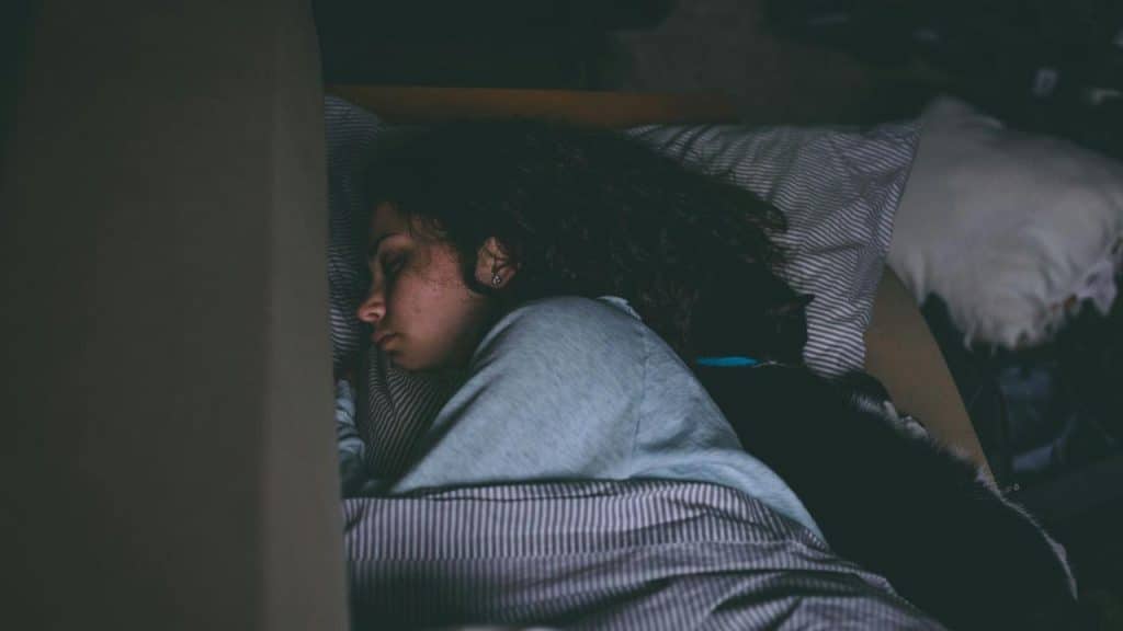 A person sleeping on their side with a cat curled up behind them.