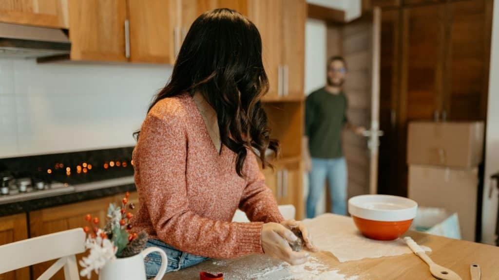 Woman in kitchen preparing food; man standing by an open door in the background.