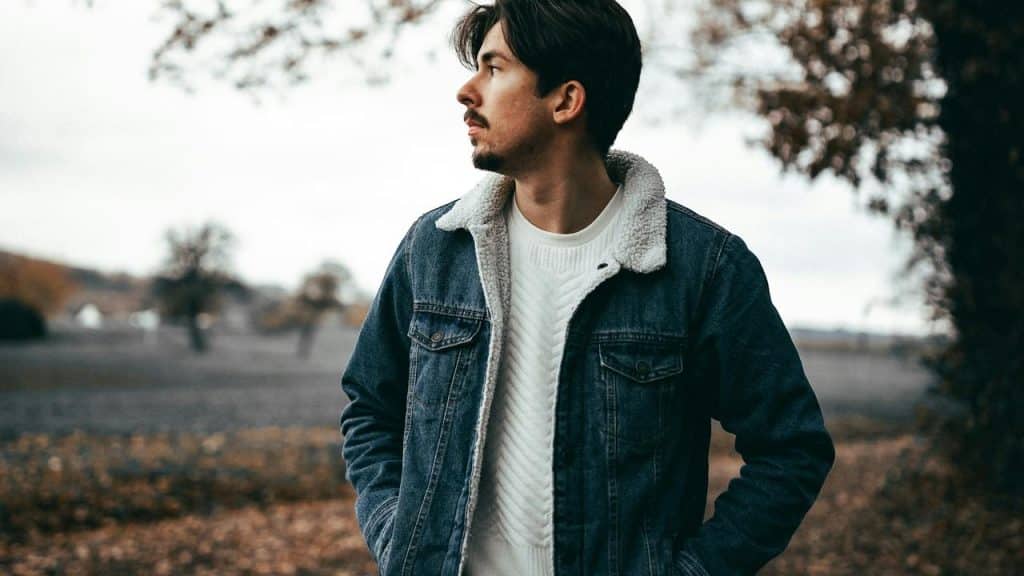 A person wearing a denim jacket standing outdoors and looking to the side.