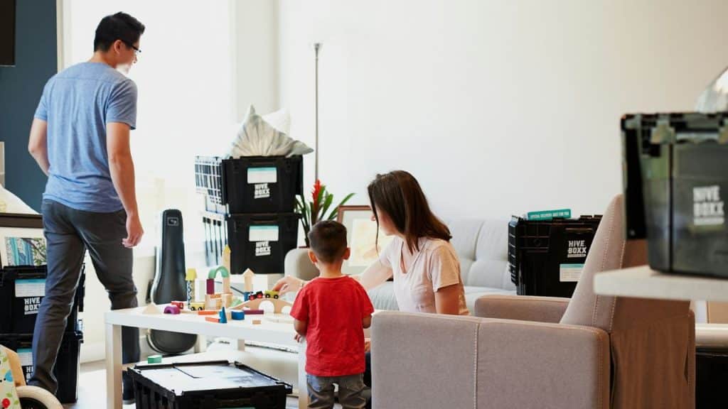 Family in a living room; mother and child playing near moving boxes, man stands nearby.