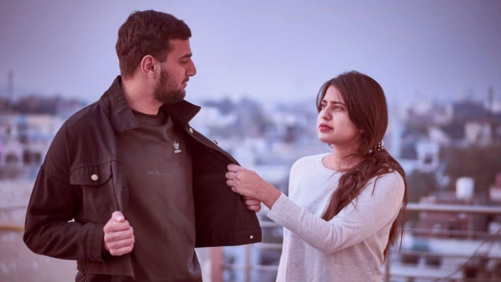 A young woman with a tearful expression touches a man's jacket outdoors.