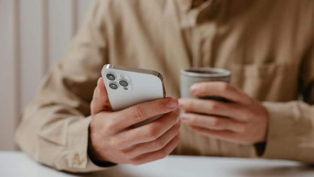 A person holding a smartphone and a cup of coffee.