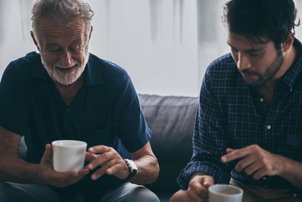 A man talking to his adult son while having a coffee together.