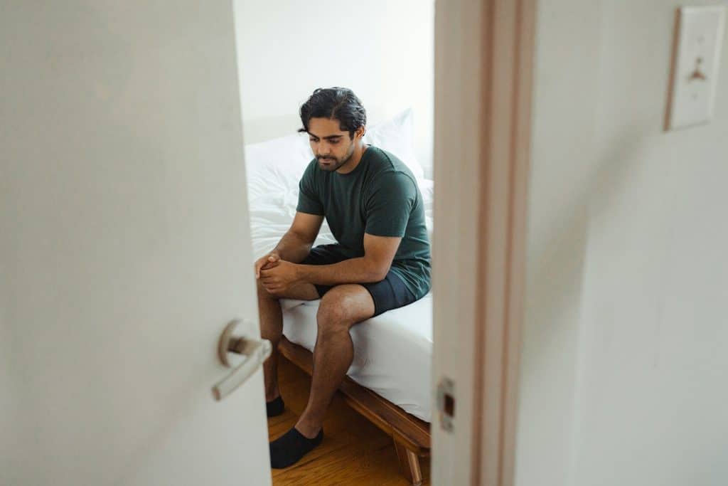 A man sitting on the bed, looking sad.