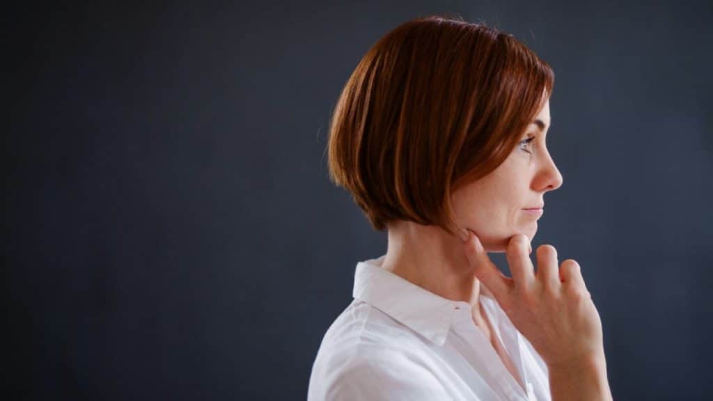 Woman with short reddish-brown hair in a white shirt, holding her chin in profile.