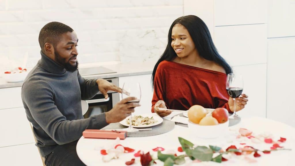 A couple enjoying dinner and wine together at a table decorated with rose petals.