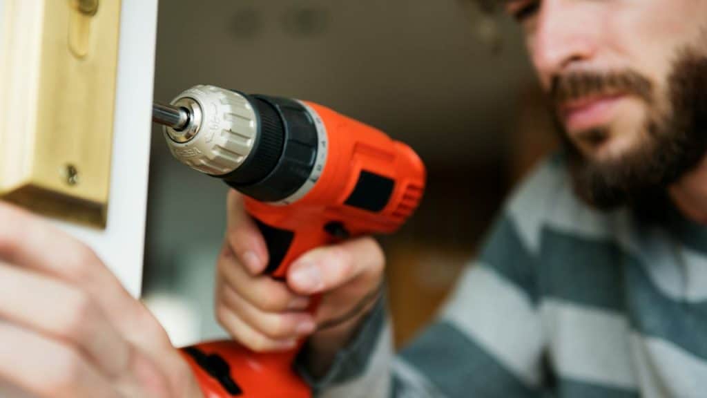 Man installing or fixing a door lock with an orange and black power drill.