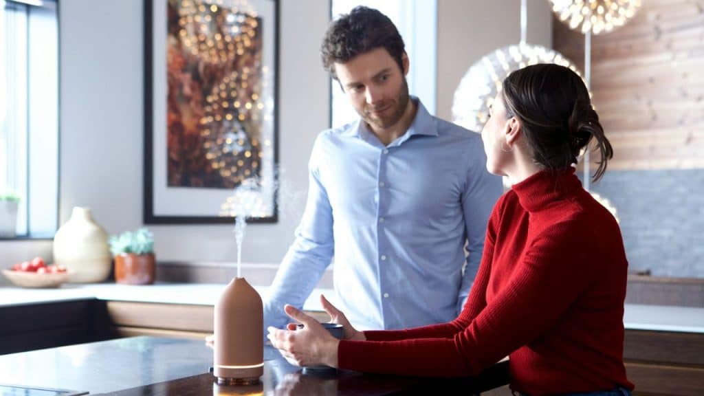 Man in blue shirt standing while woman in red sweater sits and gestures.