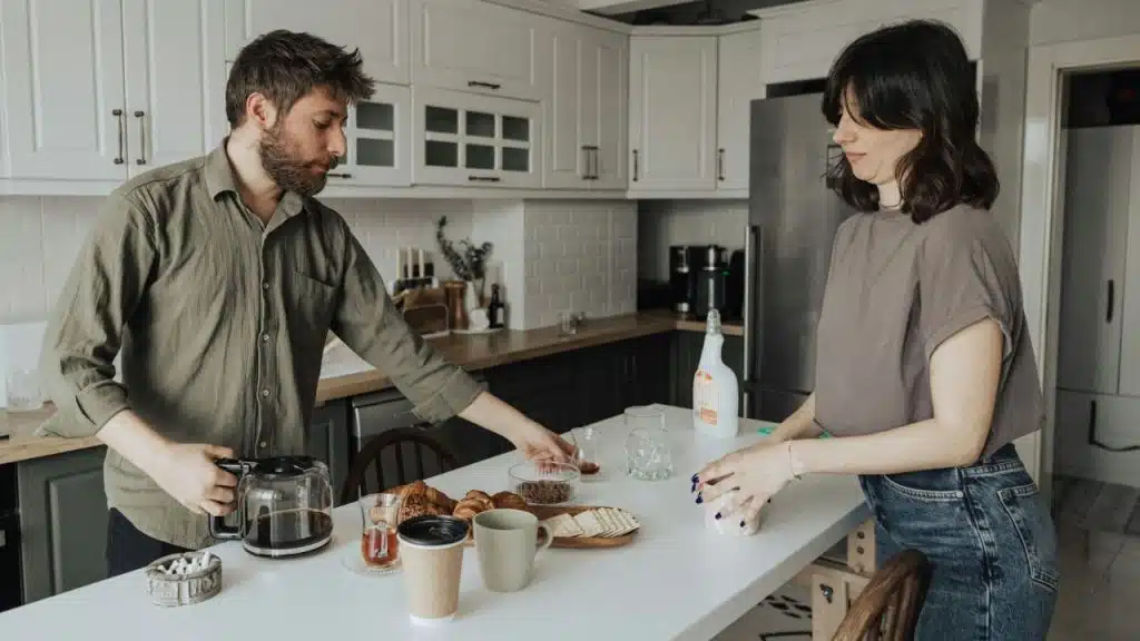 A man and woman prepare food and drinks on a white kitchen counter.