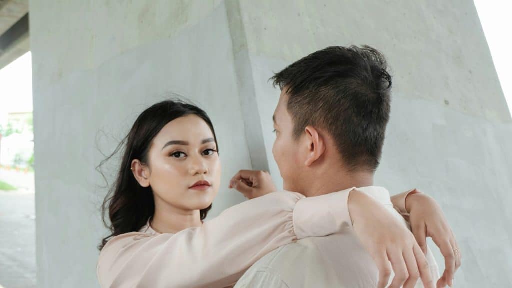 A woman leaning her arms on the shoulders of her husband, who is looking at her.